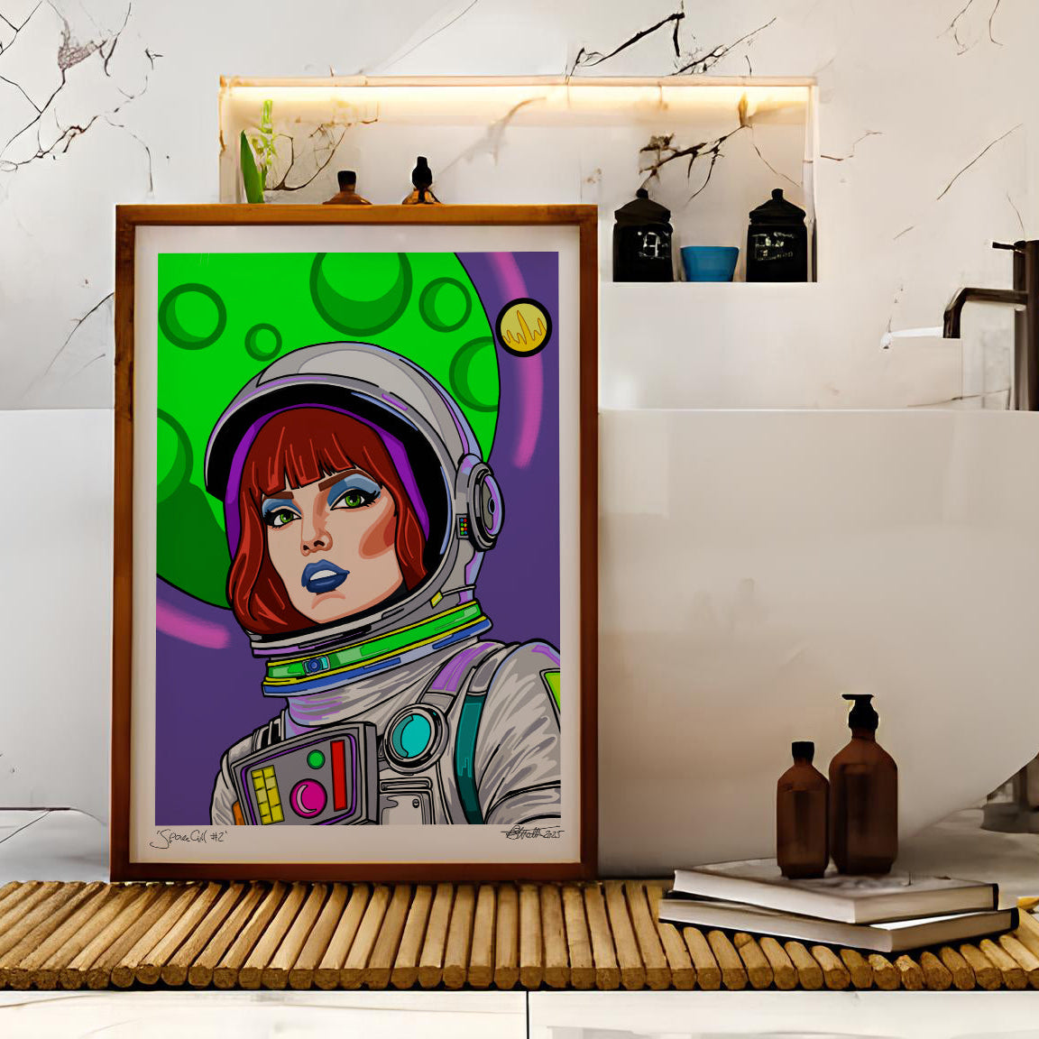 A framed pop-art print of an astronaut with red hair and blue lips, set against a colorful green and purple background, displayed on a bamboo mat in front of a white freestanding bathtub in a marble bathroom.