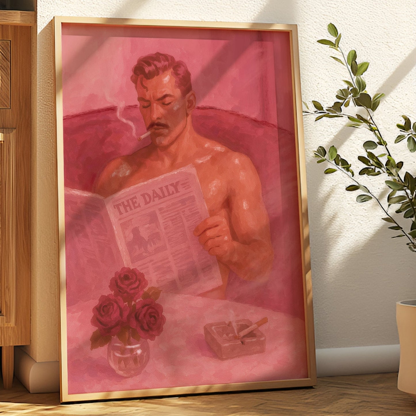 Framed artwork of a shirtless man reading a newspaper with roses and a cigarette on a pink background, placed indoors.