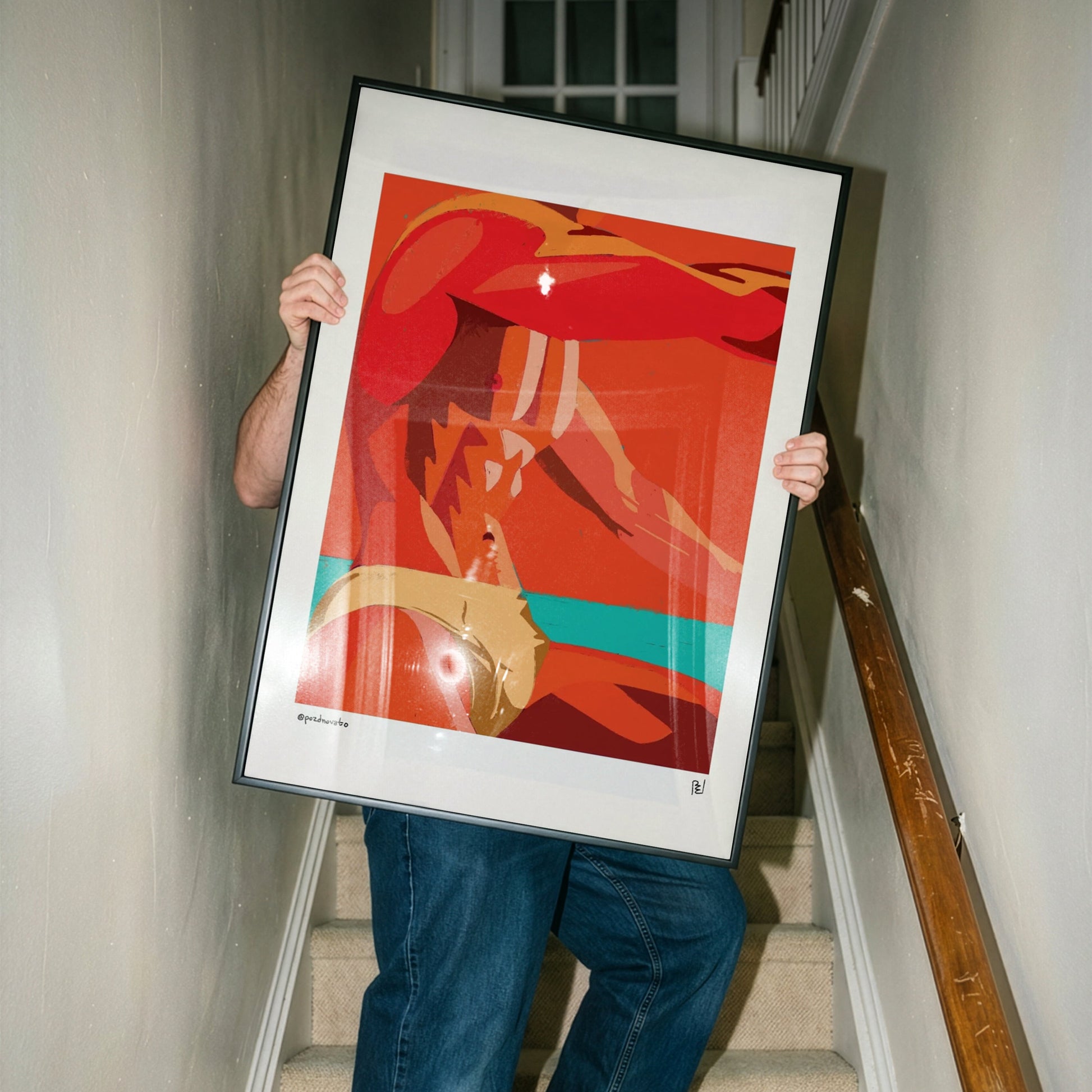 A person holding a large framed abstract art print with a bold red, orange, and teal design, walking down a carpeted staircase in a home interior.