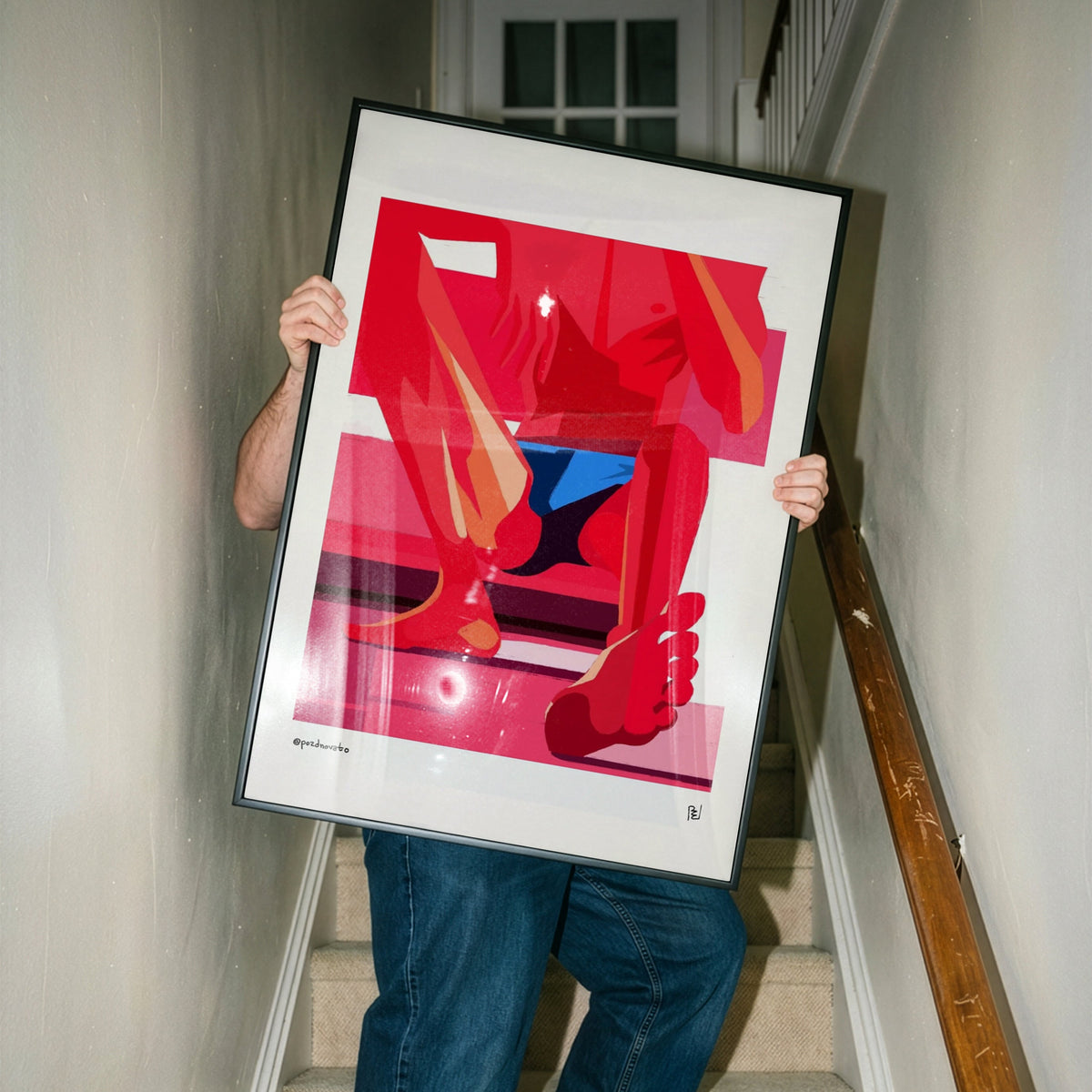 A person holding a large framed art print featuring a bold abstract red, pink, and blue composition, standing on a carpeted staircase indoors.