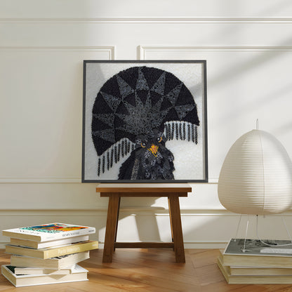 A framed art print of a black bird with a large fan-like crest, displayed on a wooden stool in a styled room with books and a lamp.
