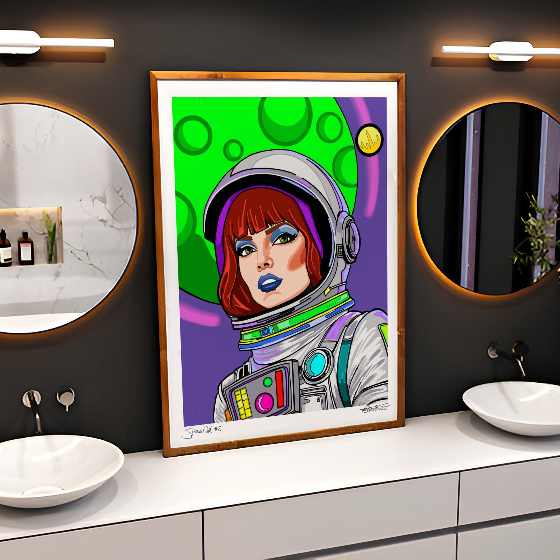 A framed pop-art print of an astronaut with red hair and blue lips, set against a colorful green and purple background, displayed on a bathroom wall above a double-sink vanity.