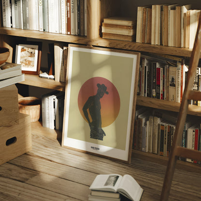 Bookshelf with books and a framed picture of a silhouette against a sunset sky.