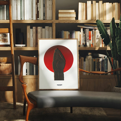 Framed artwork of a red circle with a black silhouette on a white background, displayed in a room with bookshelves and a plant.