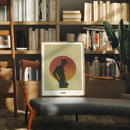 Framed artwork of a silhouette against a sunset background in a cozy room with bookshelves and a plant.