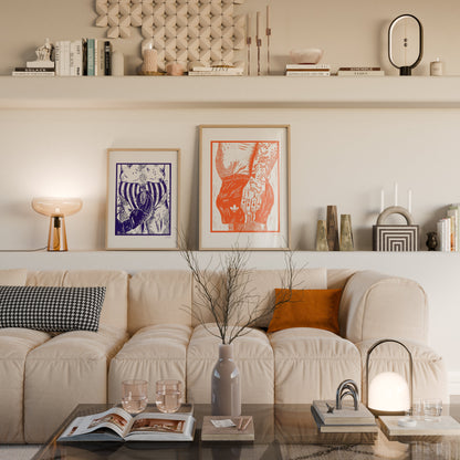A styled living room interior featuring a cream boucle sofa with accent pillows, two framed art prints on the wall, open shelving with decor, and a glass coffee table in the foreground.