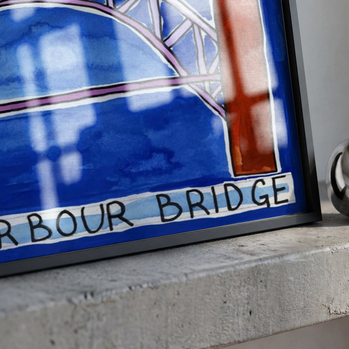 A framed art print depicting a stylized blue and white illustration of the Harbour Bridge with black lettering, resting on a textured concrete ledge next to a polished silver bell.