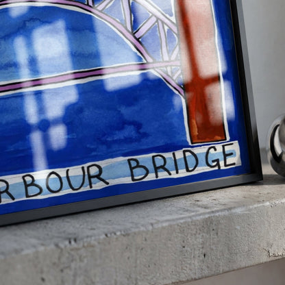 A framed art print depicting a stylized blue and white illustration of the Harbour Bridge with black lettering, resting on a textured concrete ledge next to a polished silver bell.