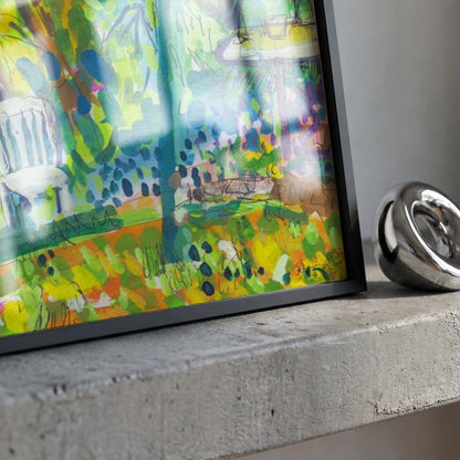 A framed abstract landscape art print with a colorful green, yellow, and blue painting, displayed on a concrete ledge next to a polished silver metallic ring.
