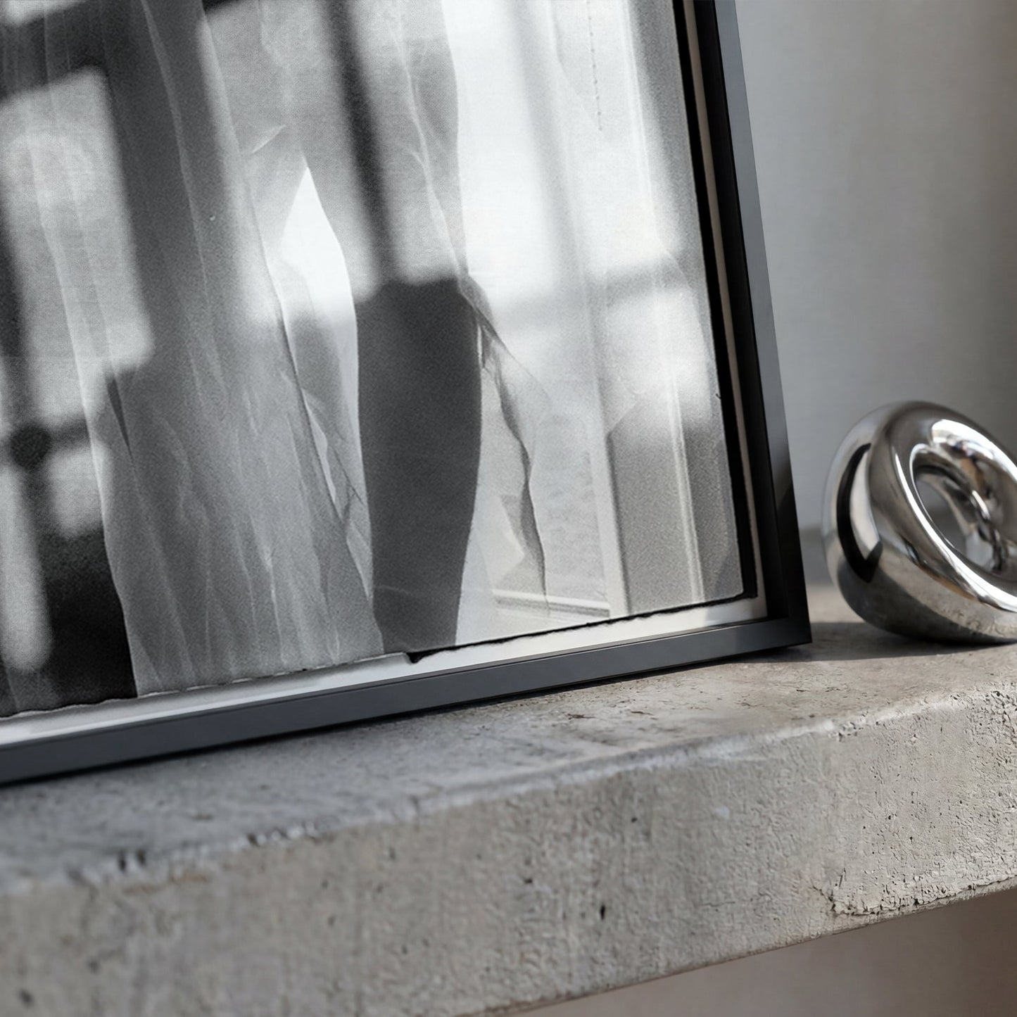 A polished metallic silver ring-shaped decorative object resting on a textured concrete ledge next to a large framed black-and-white photograph.
