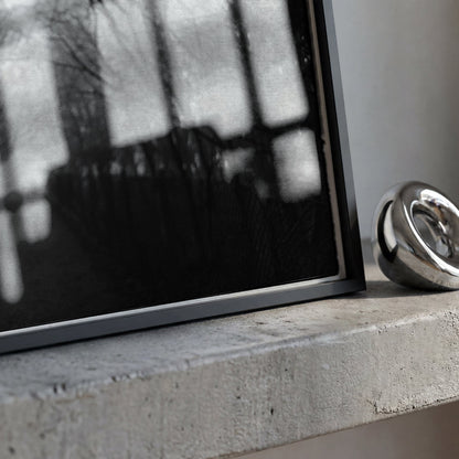 A polished silver metallic ring-shaped object, possibly a decorative sculpture or candle holder, resting on a textured concrete ledge next to a framed black-and-white photograph.