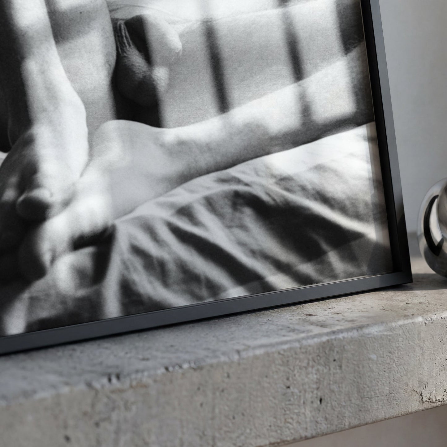 A framed black and white photograph leaning on a concrete ledge next to a polished metallic ring-shaped object.