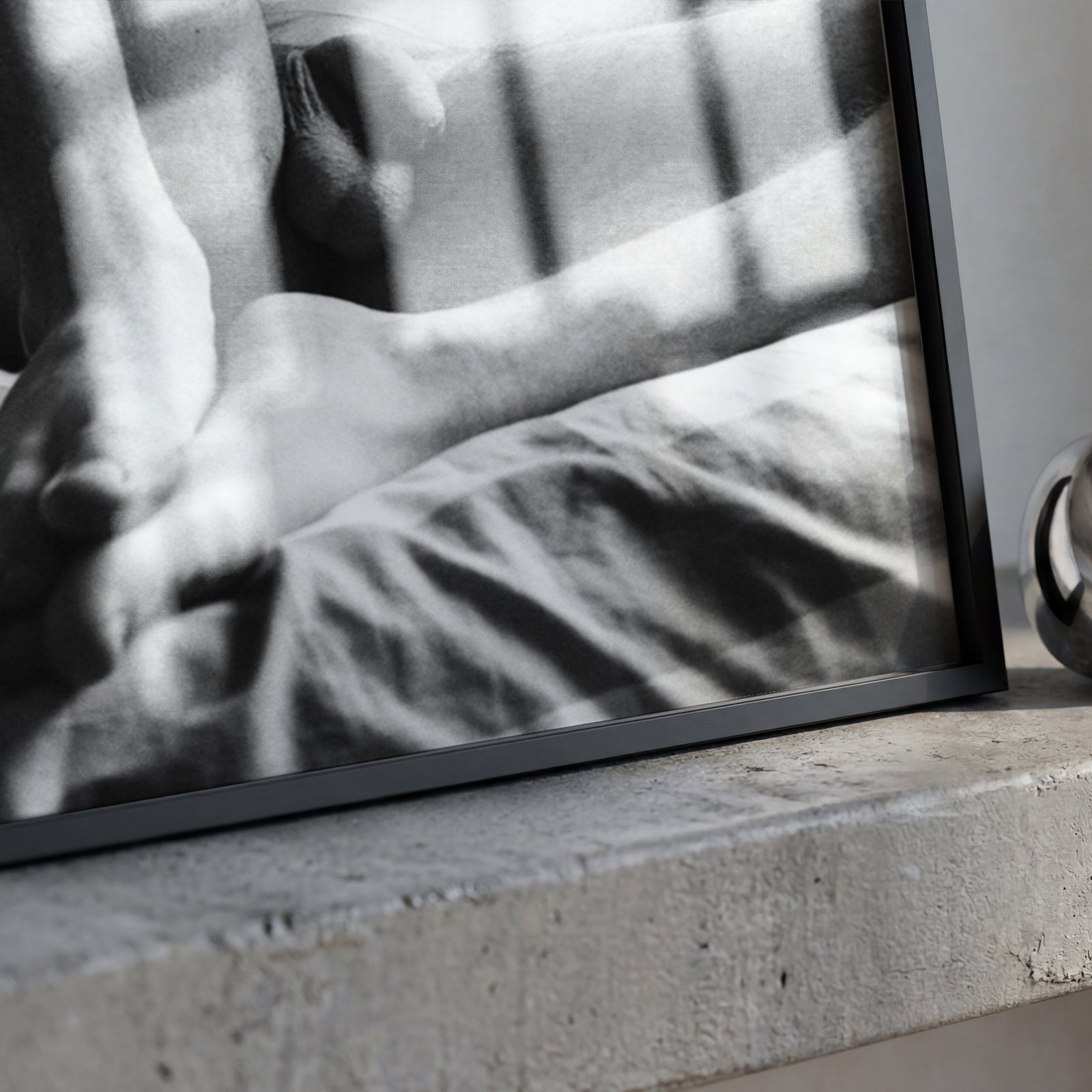 A framed black and white photograph leaning on a concrete ledge next to a polished metallic ring-shaped object.