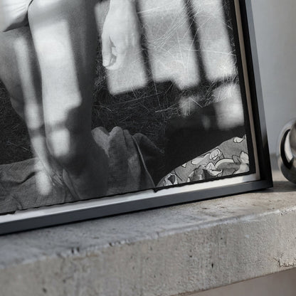 A black-framed black and white art print leaning against a concrete ledge, next to a polished silver metallic ring-shaped object.