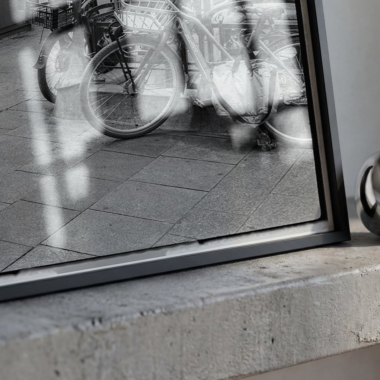 A framed black and white photograph leaning on a concrete ledge next to a shiny metallic ring-shaped object.