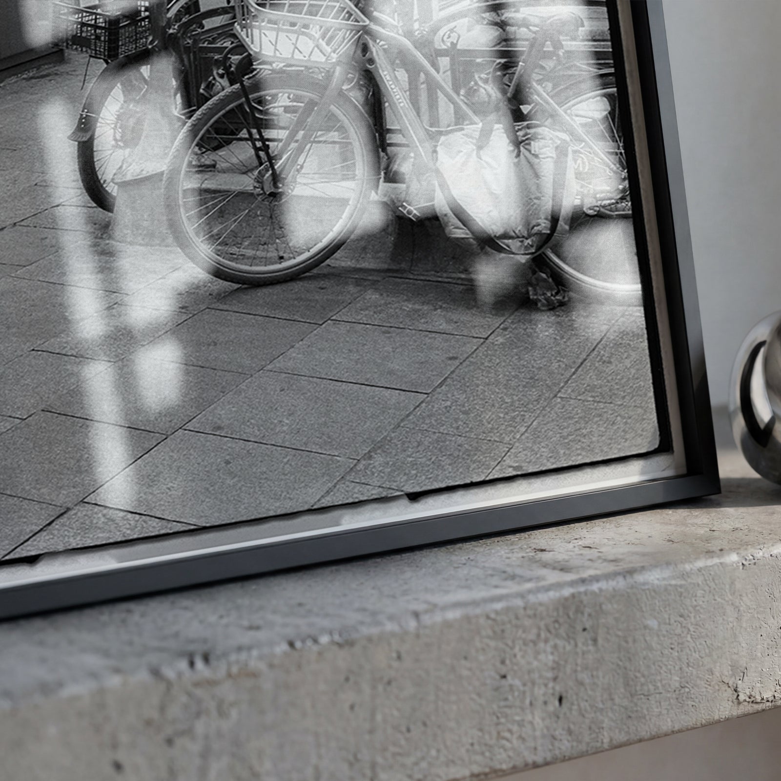 A framed black and white photograph leaning on a concrete ledge next to a shiny metallic ring-shaped object.